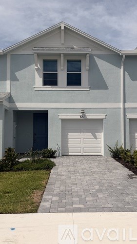 A house with a grey garage door and a brick pathway leading to it.
