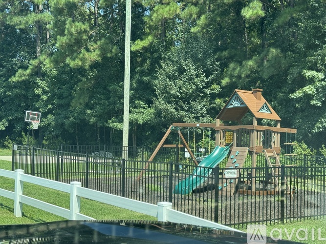 A playground with a wooden structure and a green slide is surrounded by a white fence.