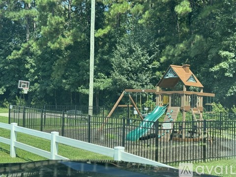 A playground with a wooden structure and a green slide is surrounded by a white fence.