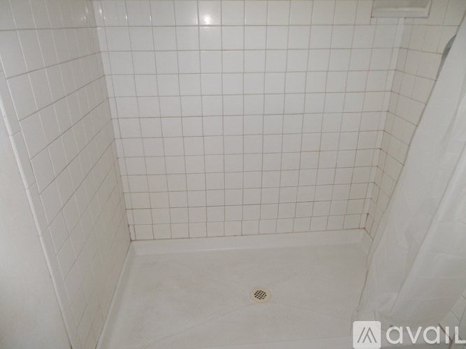 A white tiled shower with a drain in the middle.