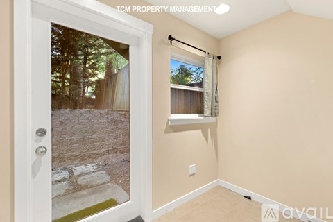 A room with a door leading outside and a window with a view of trees.