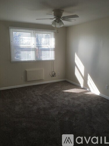 A room with a carpeted floor, a ceiling fan, and a window with blinds.