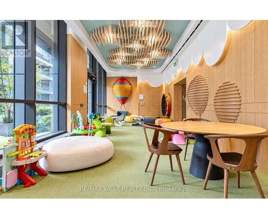 A room with a wooden table and chairs, a green carpet, and a colorful play area with a slide.