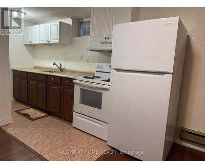 A white refrigerator stands in a kitchen with brown cabinets and a tiled floor.