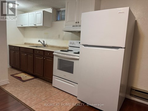 A white refrigerator stands in a kitchen with brown cabinets and a tiled floor.