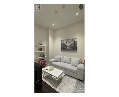 A living room with a grey couch, a coffee table, and a wall with a picture and a shelf with toys.