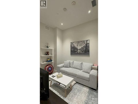 A living room with a grey couch, a coffee table, and a wall with a picture and a shelf with toys.