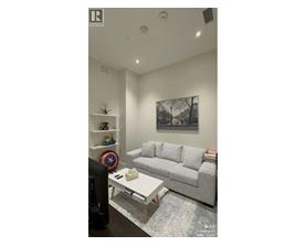 A living room with a grey couch, a coffee table, and a wall with a picture and a shelf with toys.