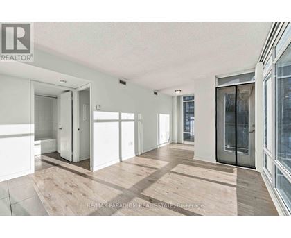 A spacious room with wooden flooring and white walls, featuring a sliding glass door.