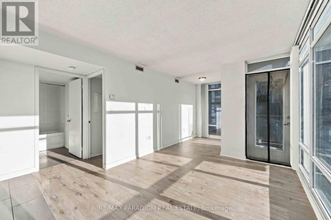 A spacious room with wooden flooring and white walls, featuring a sliding glass door.