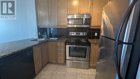 A kitchen with a stainless steel refrigerator and black countertops.