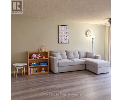 A living room with a grey sofa, a wooden shelf with toys, and a white table.