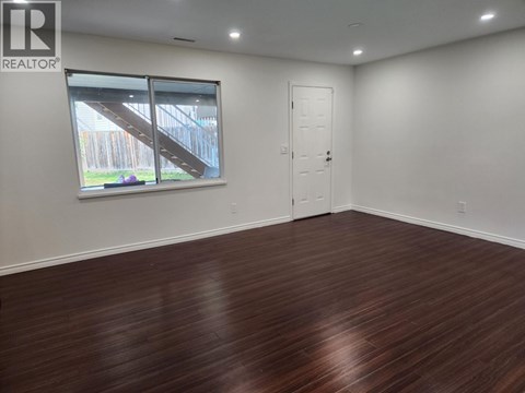 A room with wooden flooring and a window showing an outdoor staircase.