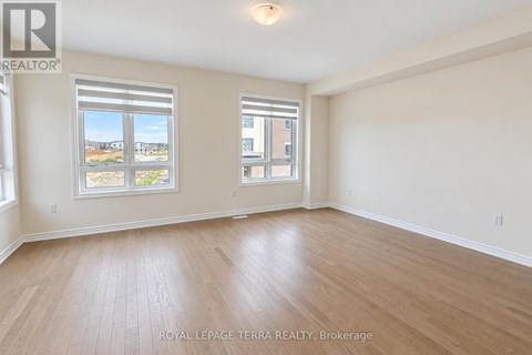 A spacious room with wooden flooring and two windows.