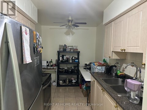 A kitchen with a refrigerator, sink, and a fan.