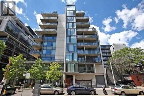 A modern multi-story building with a glass facade is surrounded by parked cars.