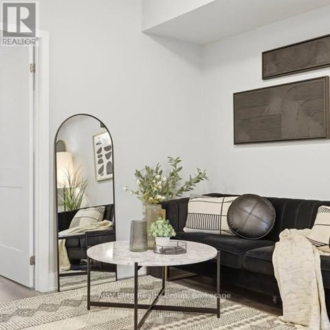 A living room with a black couch, a round mirror, and a coffee table with a vase of flowers on it.