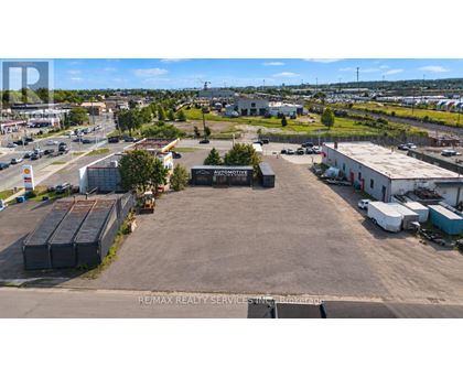 An aerial view of a commercial area with a large open space in the foreground and various buildings and vehicles in the background.