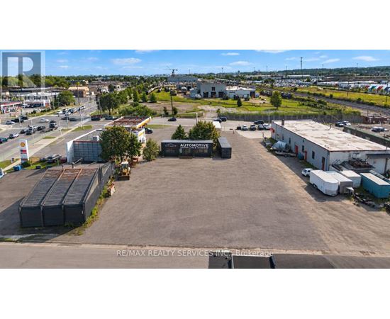 An aerial view of a commercial area with a large open space in the foreground and various buildings and vehicles in the background.