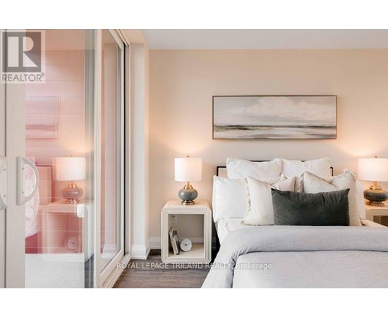 A bedroom with a large bed, two nightstands with lamps, and a painting on the wall.