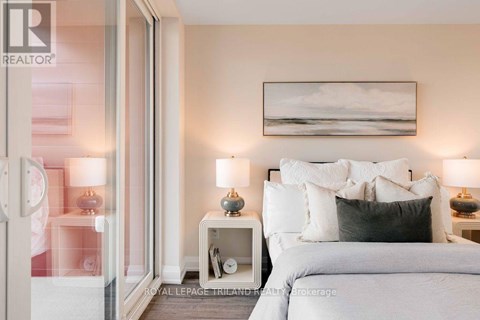 A bedroom with a large bed, two nightstands with lamps, and a painting on the wall.