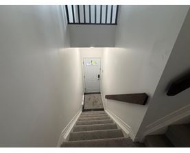 A staircase with a carpeted runner leads to a white door at the end of the hallway.
