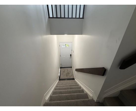 A staircase with a carpeted runner leads to a white door at the end of the hallway.