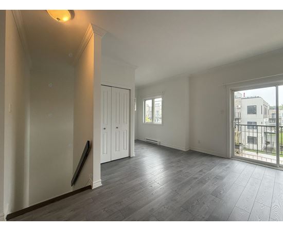 A spacious room with wooden flooring and white walls.