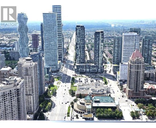 A cityscape with a mix of modern and older buildings, a large open square, and a clear sky.
