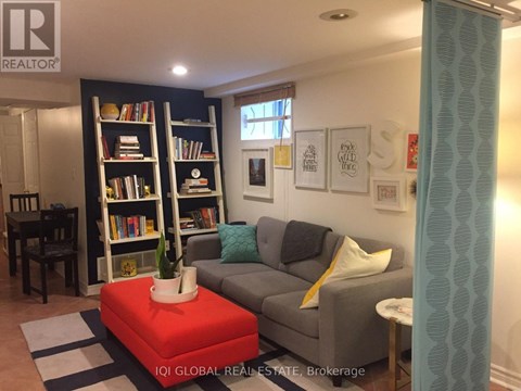 A living room with a grey couch, a red ottoman, and a bookshelf filled with books.
