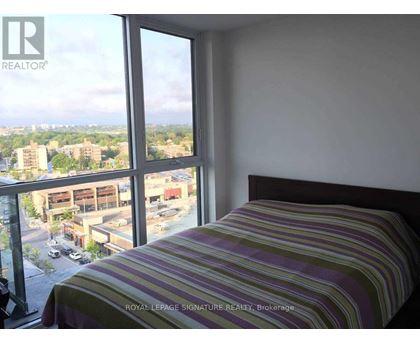 A bedroom with a striped bedspread and a large window overlooking a parking lot and buildings.
