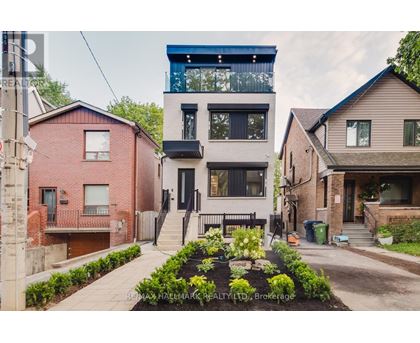 A modern two story house with a balcony on the top floor is surrounded by other houses.