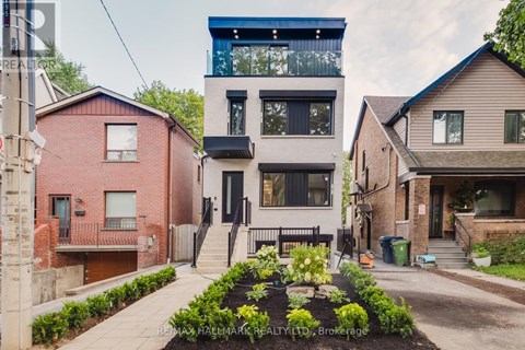 A modern two story house with a balcony on the top floor is surrounded by other houses.