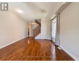 A spacious room with wooden flooring and a staircase in the background.