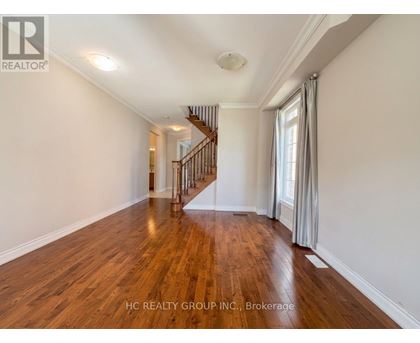 A spacious room with wooden flooring and a staircase in the background.
