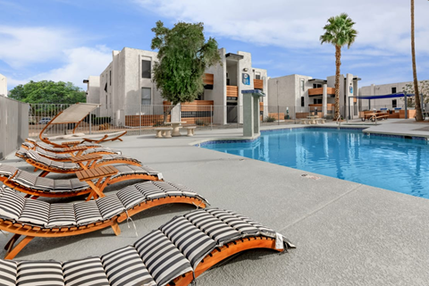 A pool area with sun loungers and a building in the background.