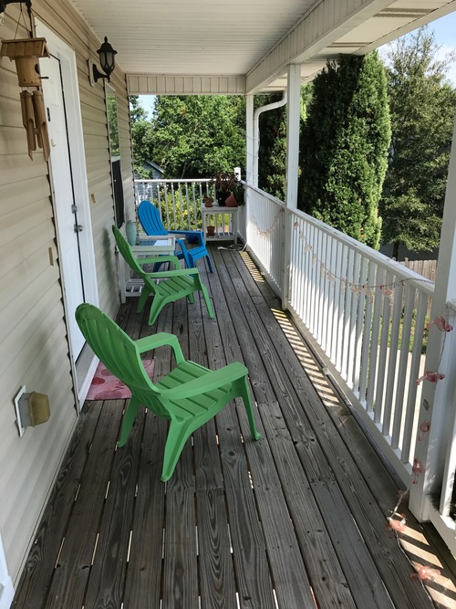 A wooden deck with two green chairs and a white railing.