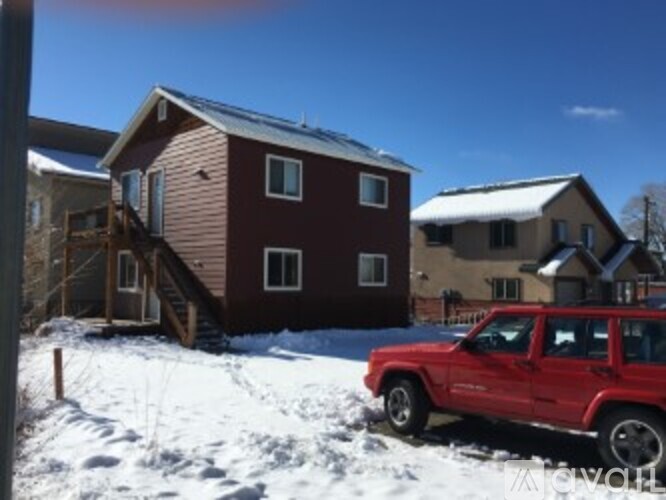 A red truck is parked in front of a house with snow on the ground.