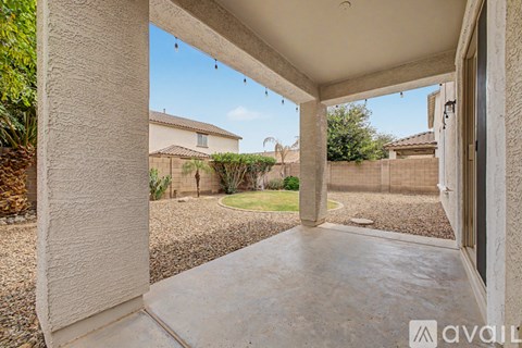 A patio area with a concrete floor and a view of a backyard with a fence and trees.