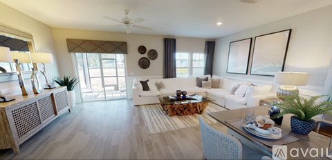 A well-lit, spacious living room with a white sofa set and a wooden coffee table.