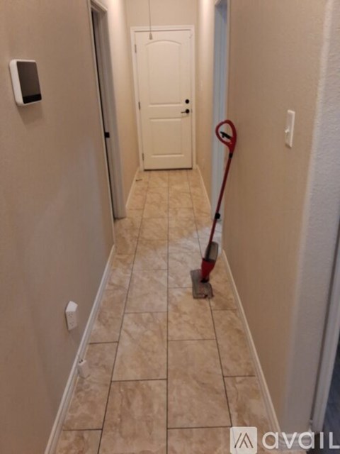 A red vacuum cleaner is on a hallway with beige tiles.