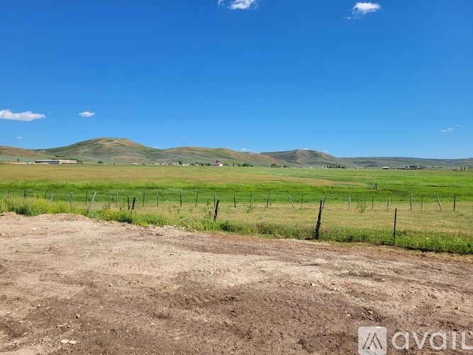 A dirt path leads to a grassy field with a fence and green hills in the distance.
