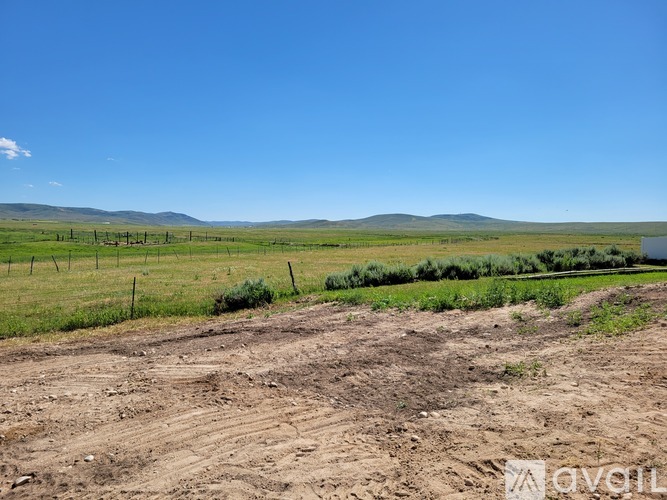 A dirt field with a fence and greenery in the distance under a blue sky.