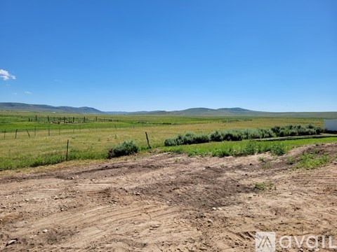 A dirt field with a fence and greenery in the distance under a blue sky.