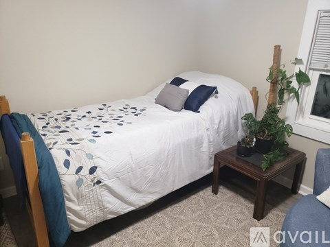 A bed with a white comforter and blue pillows is in a room with a small table beside it.