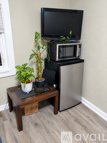 A small table with a potted plant and a microwave on top of a fridge.