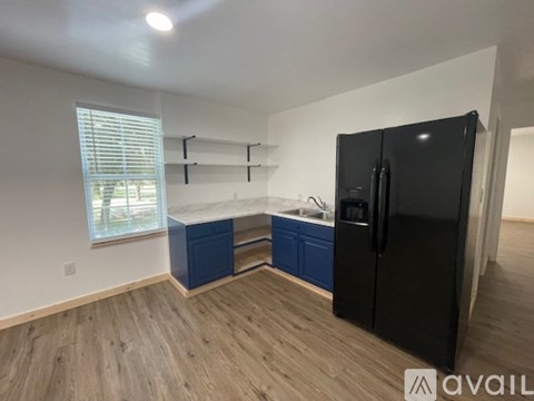 A kitchen with a black fridge, blue drawers and a window with blinds.
