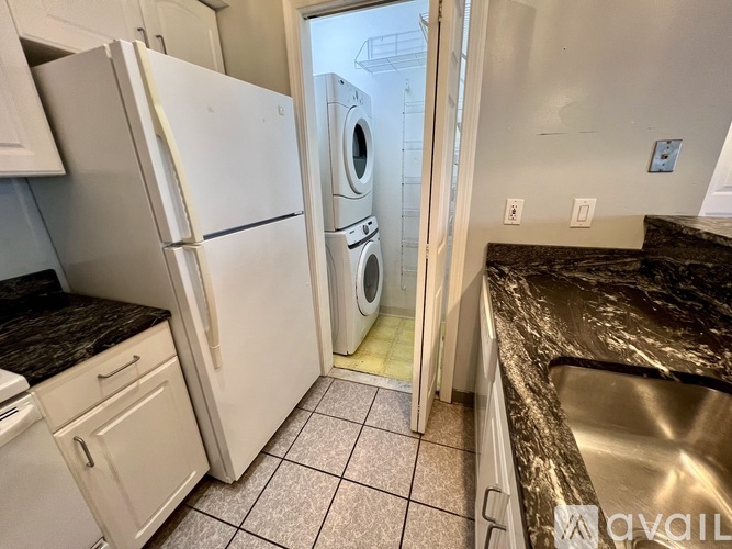 A kitchen with a white refrigerator and a washer and dryer in the doorway.