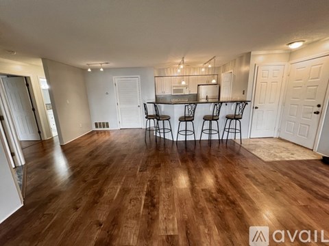 A room with wooden flooring and a bar area with four stools.