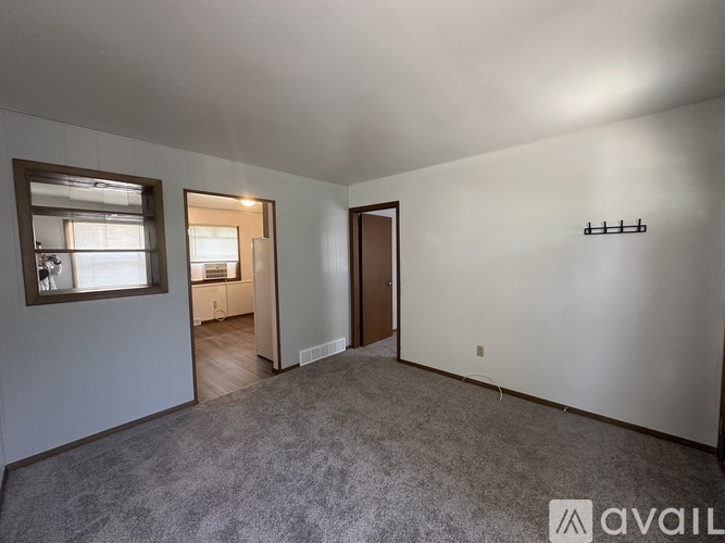A room with a carpeted floor, a door, a window, and a coat rack.